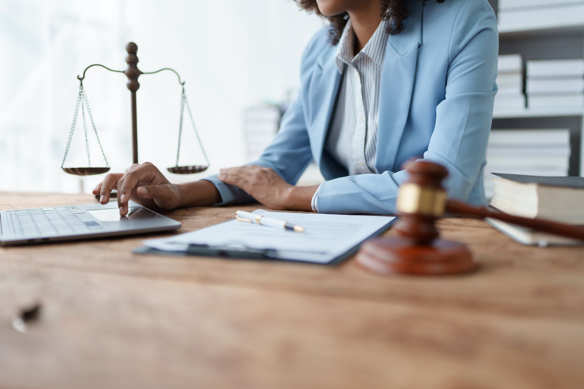 Woman in blue blazer typing on laptop, scales of justice and gavel on desk. Woman in blue blazer typing on laptop, scales of justice and gavel on desk.