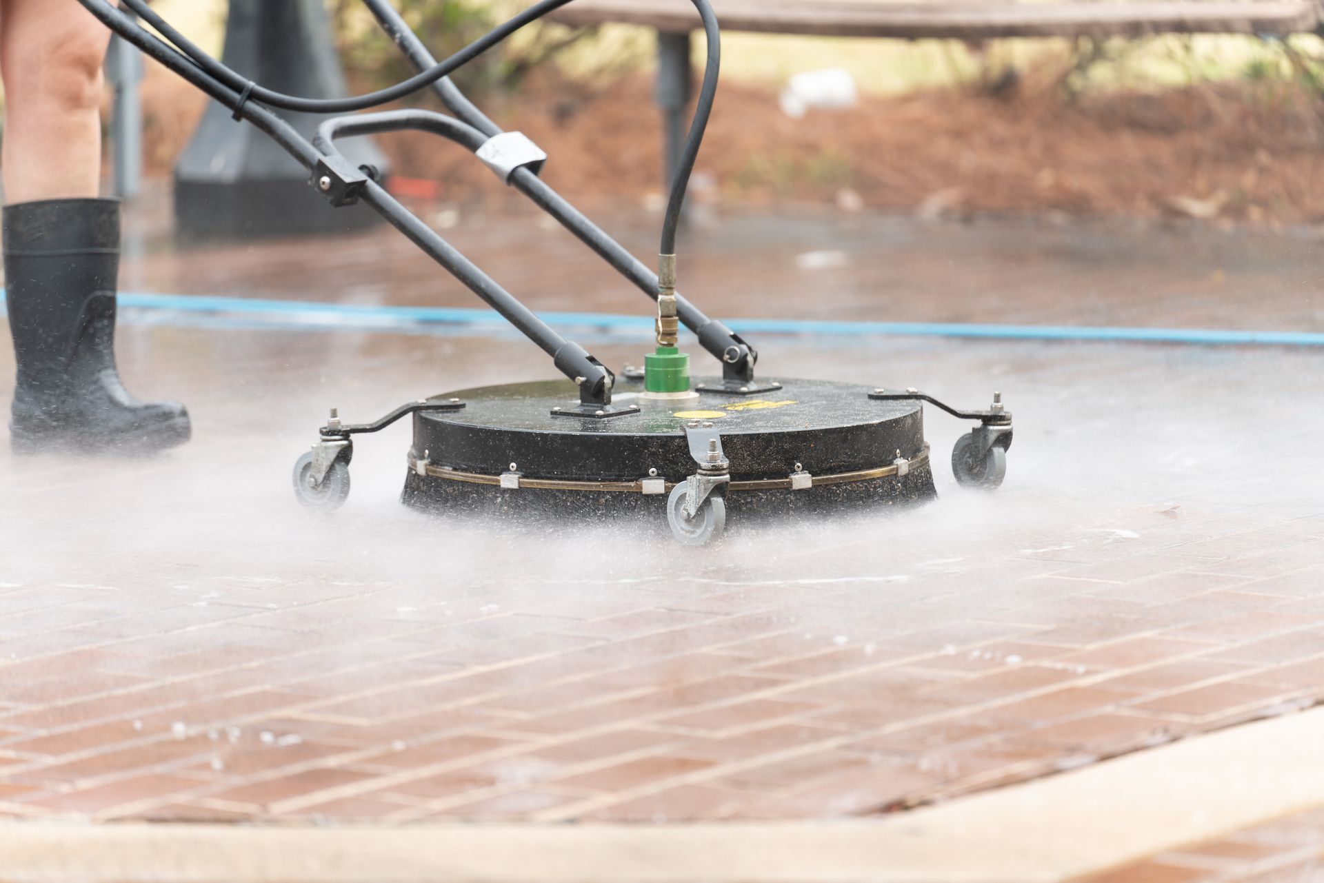Pressure washer cleaning red brick patio; person wearing boots.