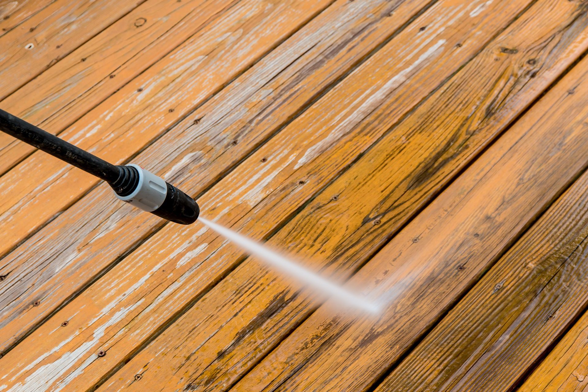 Power washer cleaning a weathered wooden deck.
