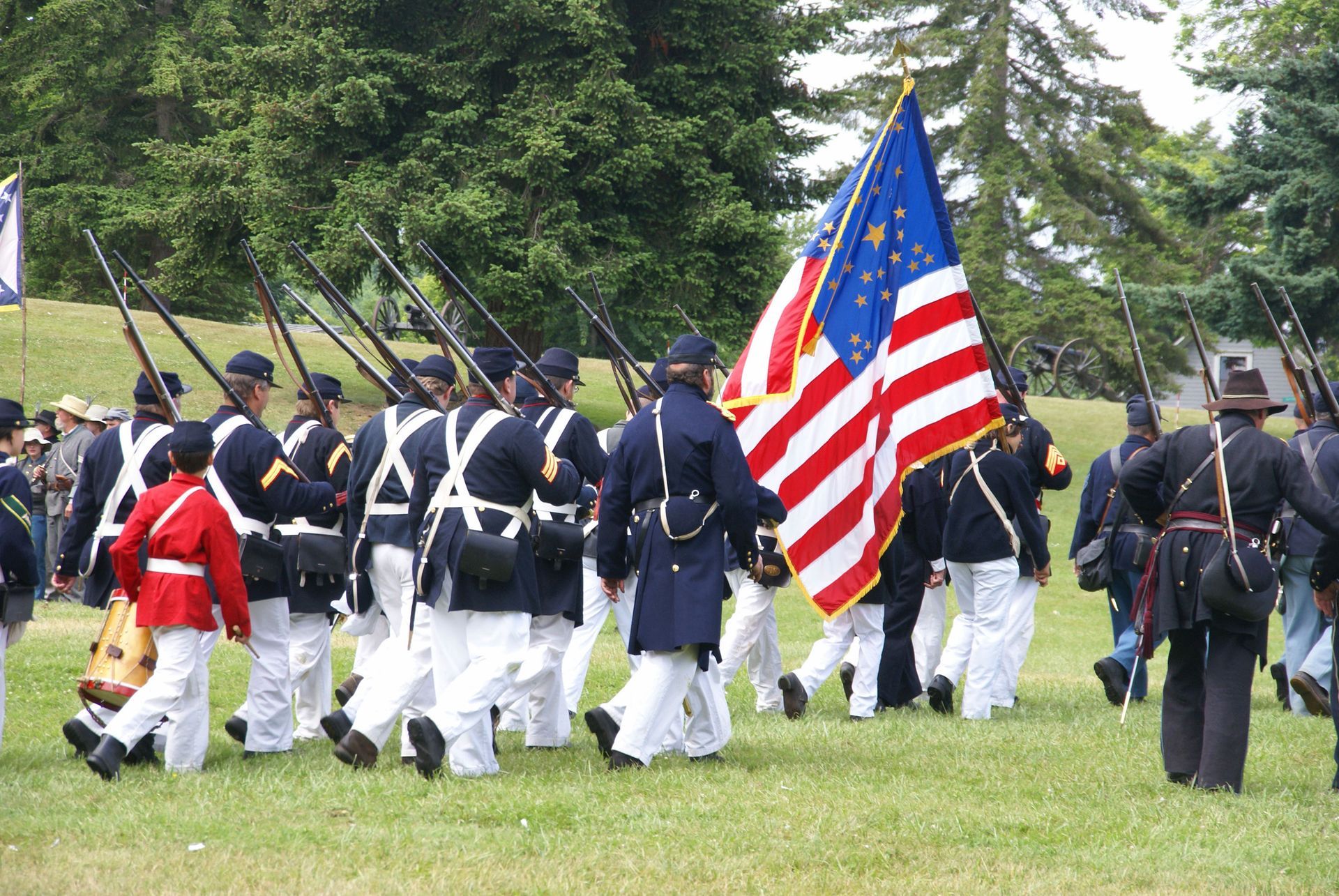 A group of soldiers marching with an American flag in a grassy field.