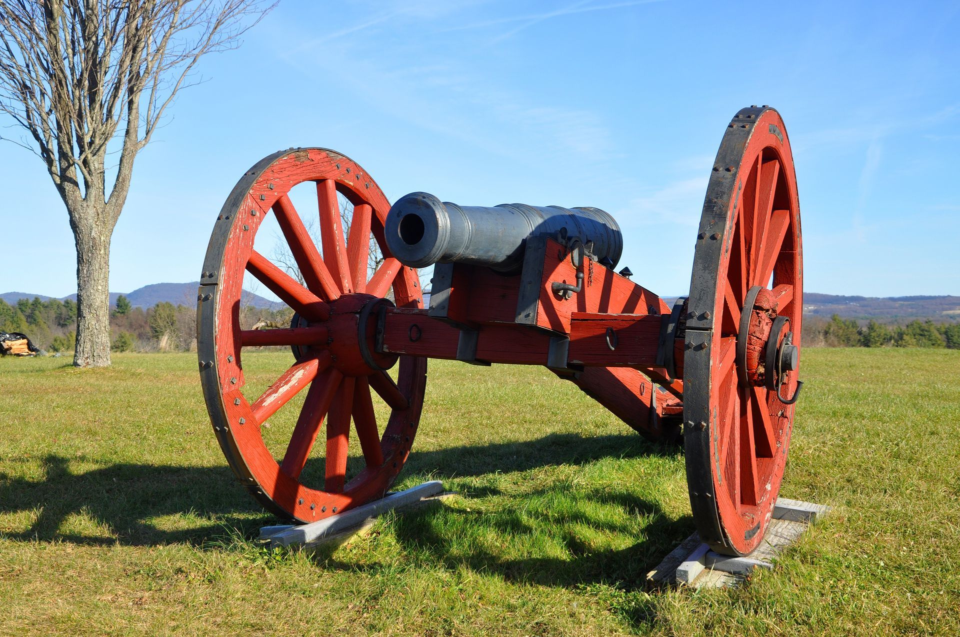 An old cannon with red wheels is sitting in a grassy field.