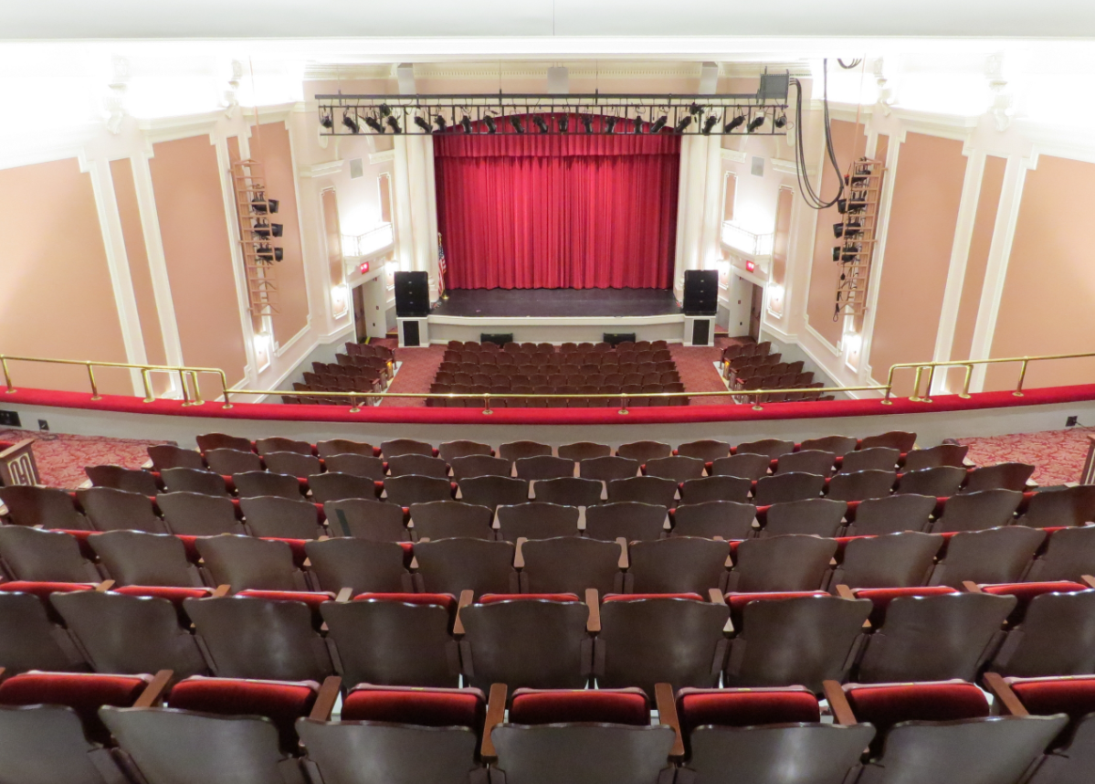 A large auditorium with rows of empty seats and a red curtain on the stage.