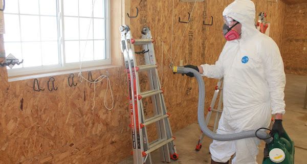 A man in a protective suit is using a vacuum cleaner in a room.