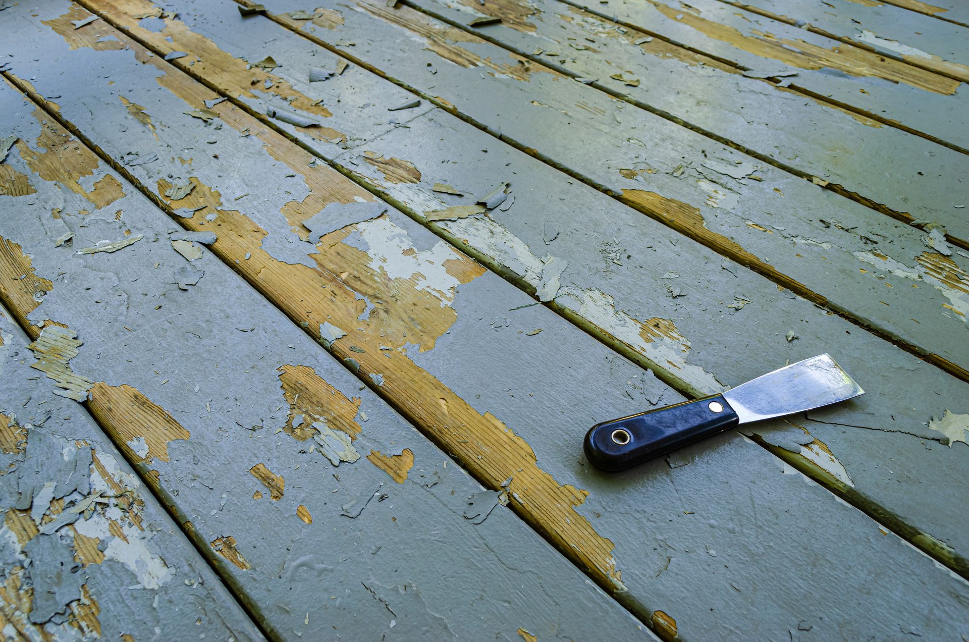 Paint scraper resting on peeling blue and yellow painted wooden planks