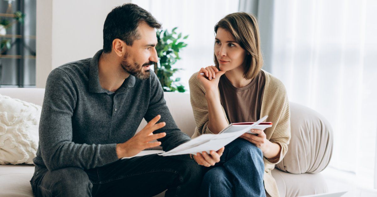 Two people sitting on a light couch with documents.