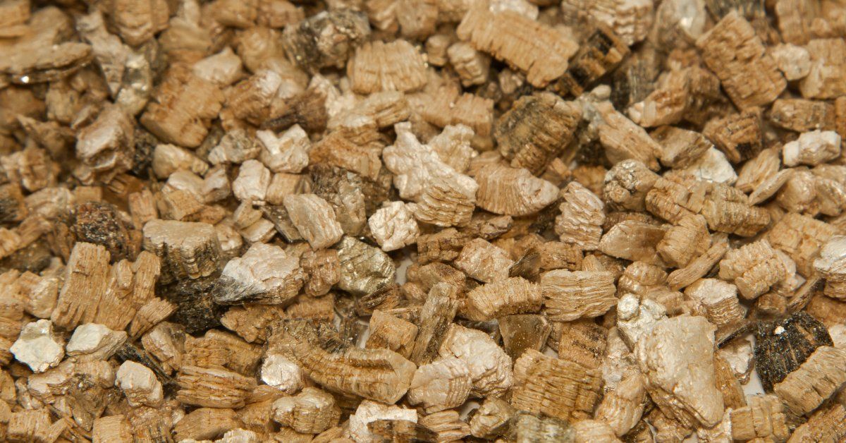 A close-up of coarse vermiculite granules spread across a flat surface, showing their layered textur