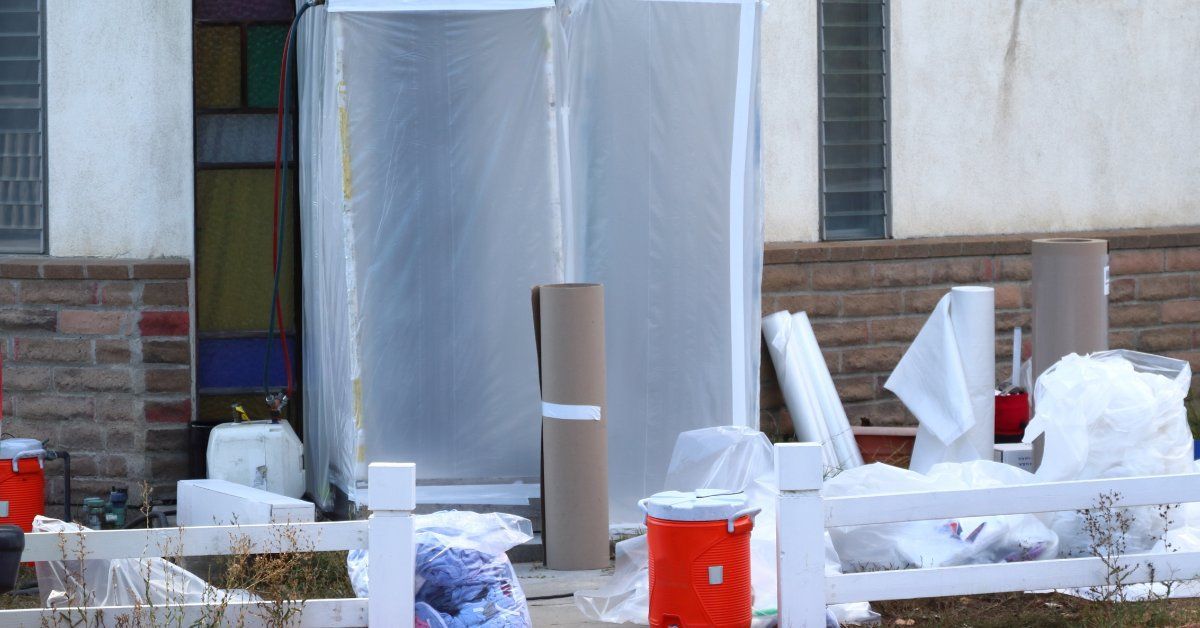 A residential entrance enclosed in translucent plastic sheeting, with bags, rolled materials, and a