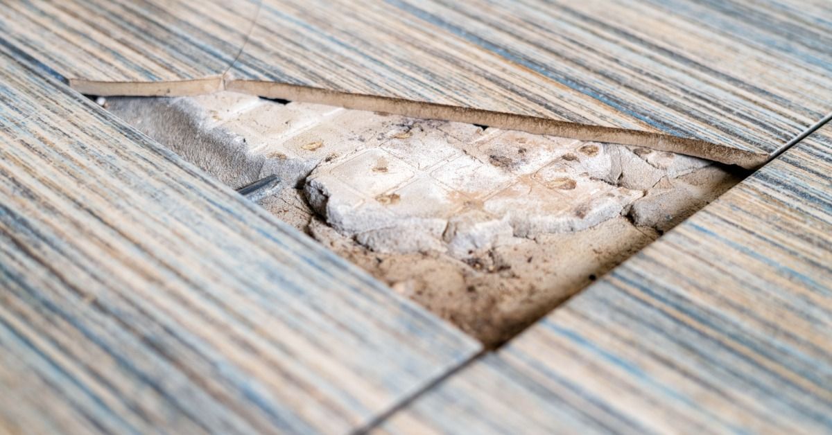 A section of broken vinyl floor tile with old adhesive and underlying tile beneath the surface.