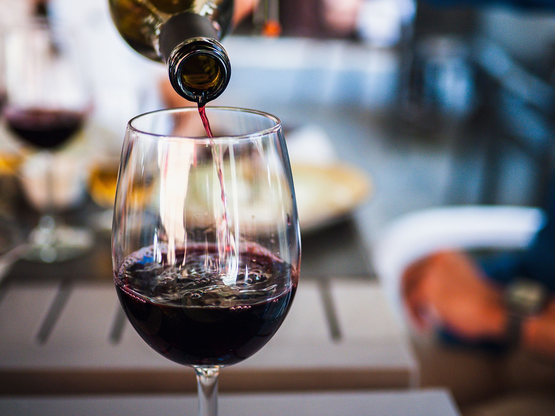 Vino rosso versato in un bicchiere da vino trasparente; ambiente sfocato del ristorante.
