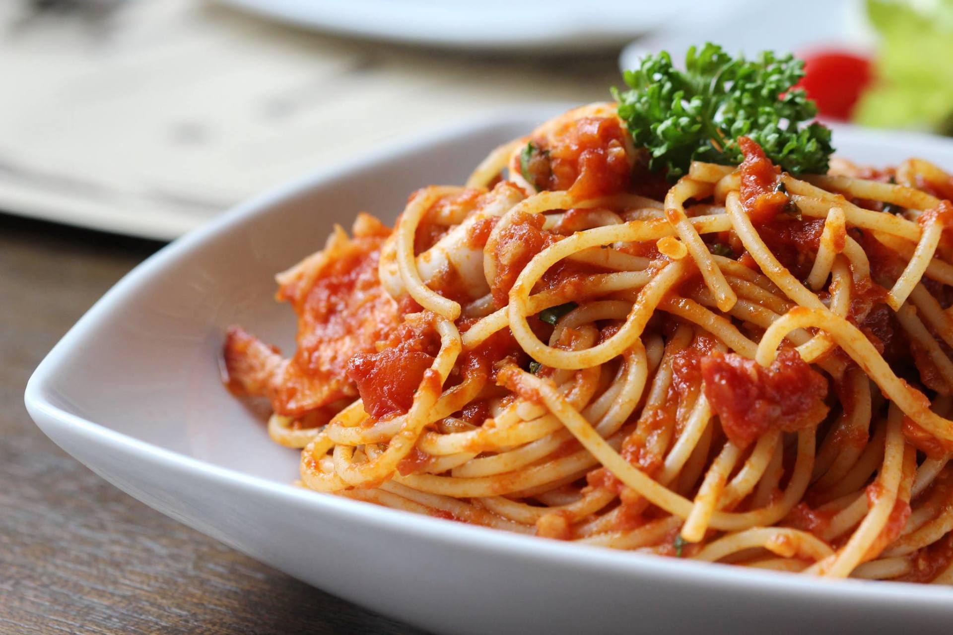 Spaghetti al sugo di pomodoro, guarnito con prezzemolo, in una ciotola quadrata bianca.