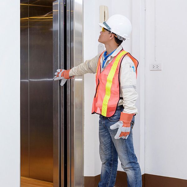 Construction worker in hard hat and safety vest opening an elevator door in a hallway