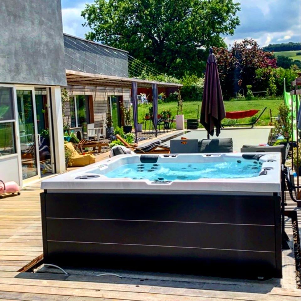 Un bain à remous est installé sur une terrasse en bois devant une maison.