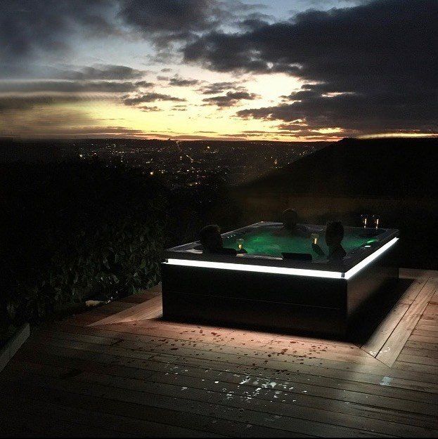 Un bain à remous est éclairé la nuit avec un coucher de soleil en arrière-plan