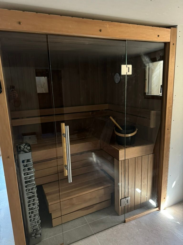 Un sauna en bois avec une porte vitrée et un seau