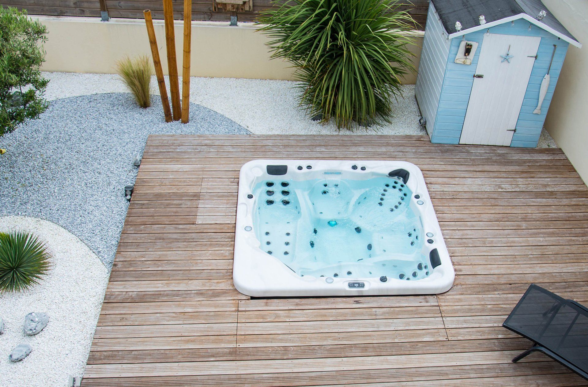Un bain à remous est posé sur une terrasse en bois à côté d'un hangar bleu.