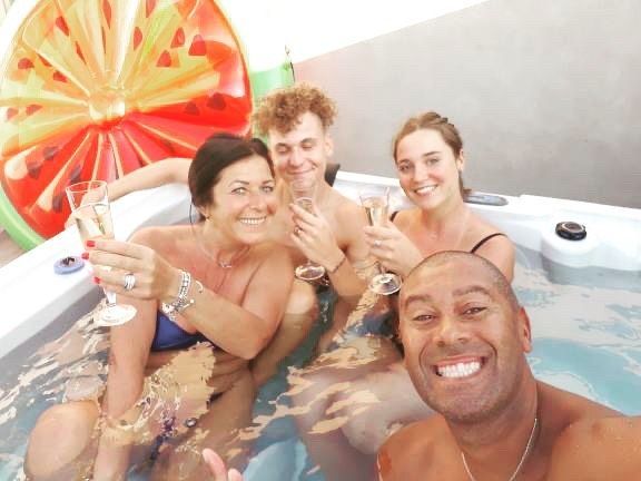 Un groupe de personnes sont assises dans un bain à remous tenant des coupes de champagne.