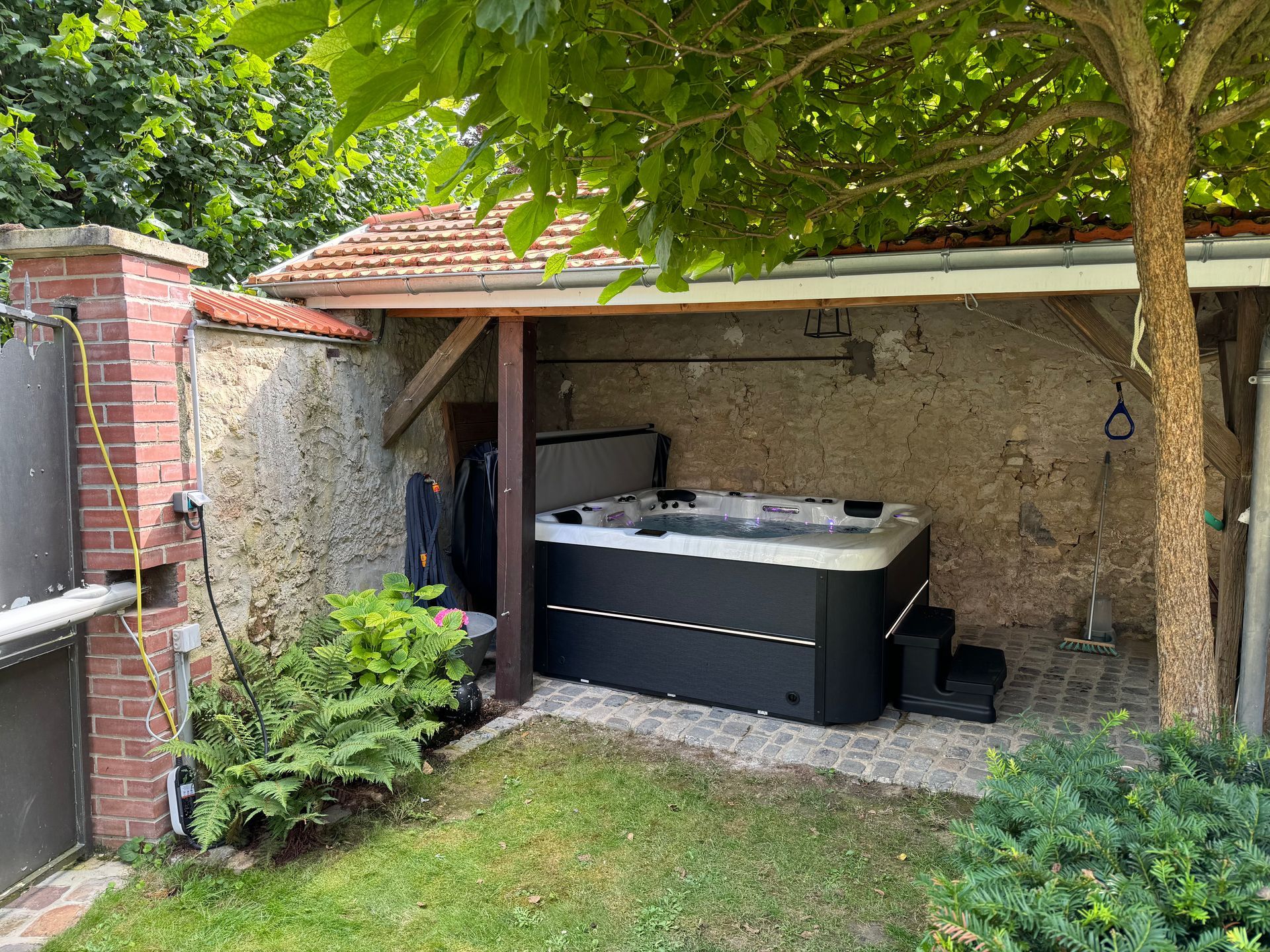 Un bain à remous est installé sous un arbre dans une cour arrière.