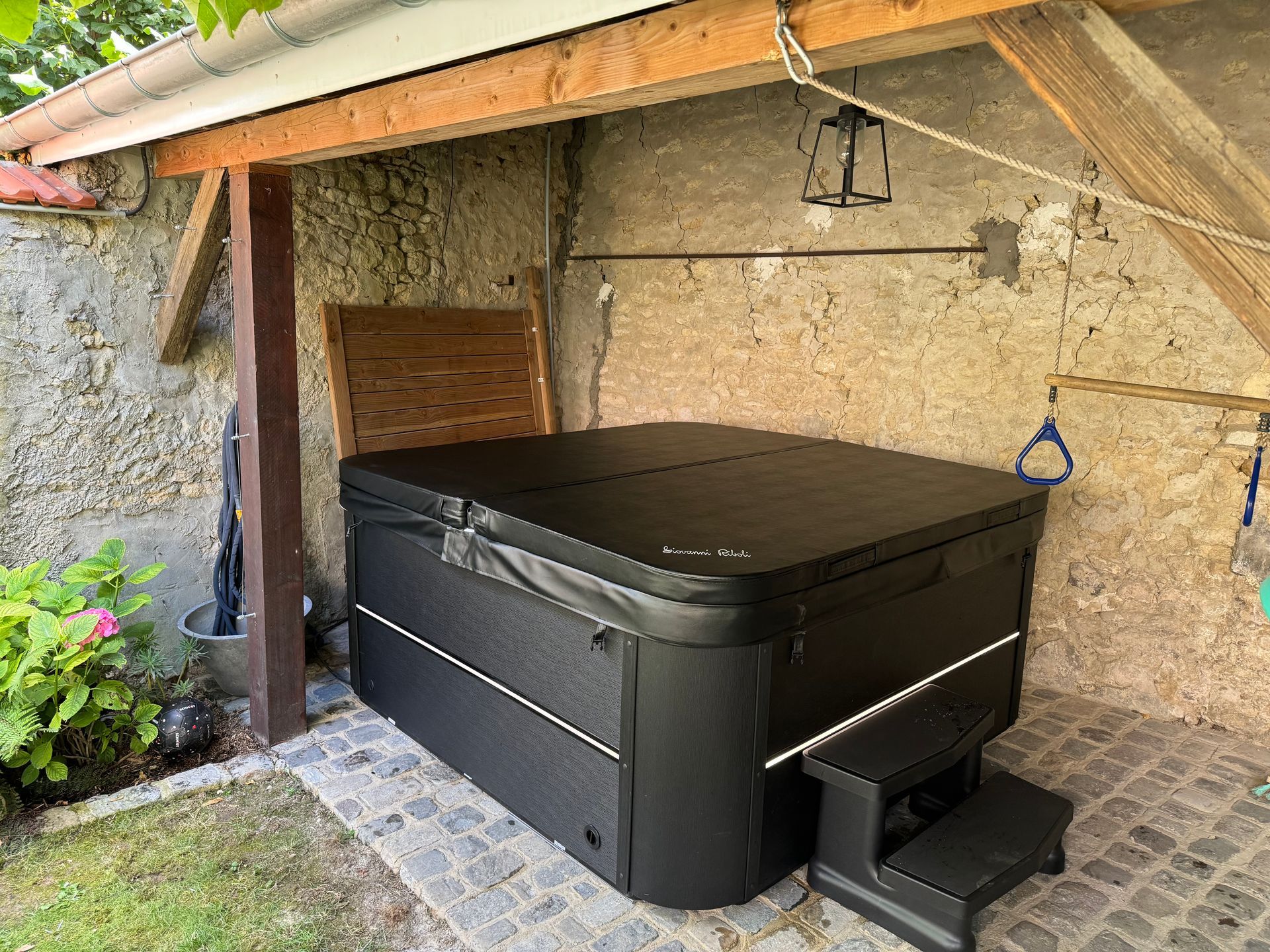Un jacuzzi noir est assis sous un toit en bois.