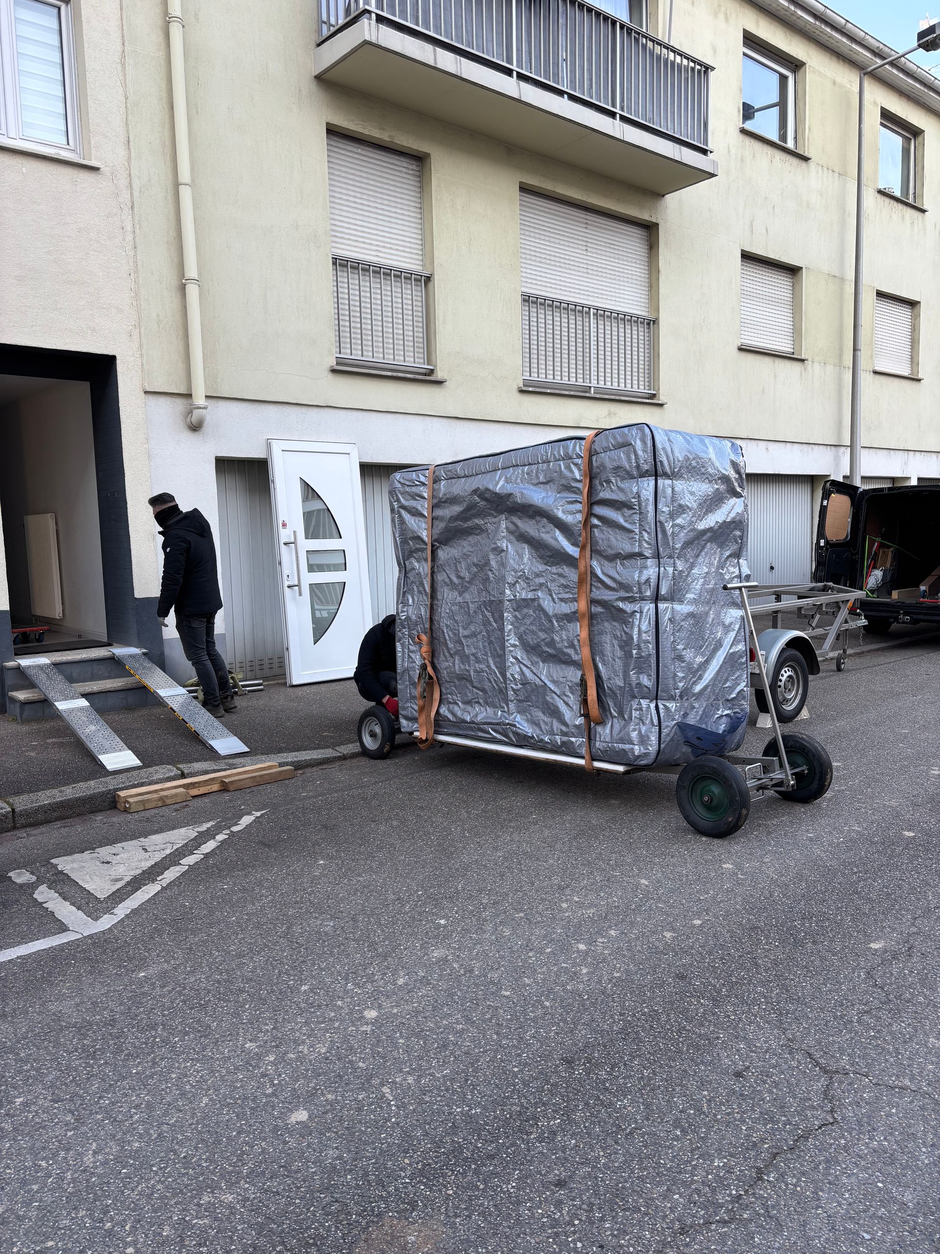 Un homme pousse un chariot avec une grande boîte dessus devant un bâtiment.