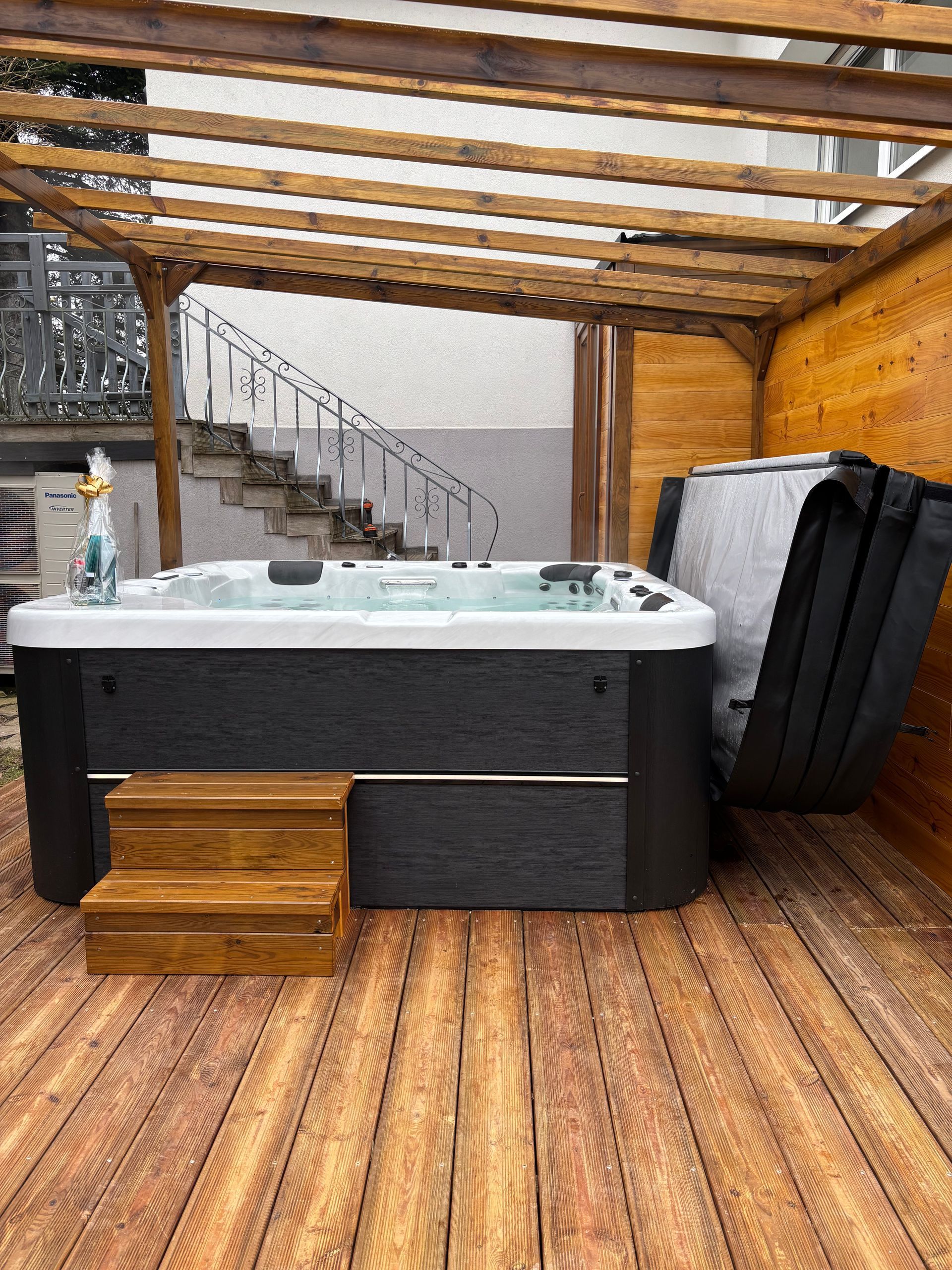 Un bain à remous est posé sur une terrasse en bois sous une pergola.
