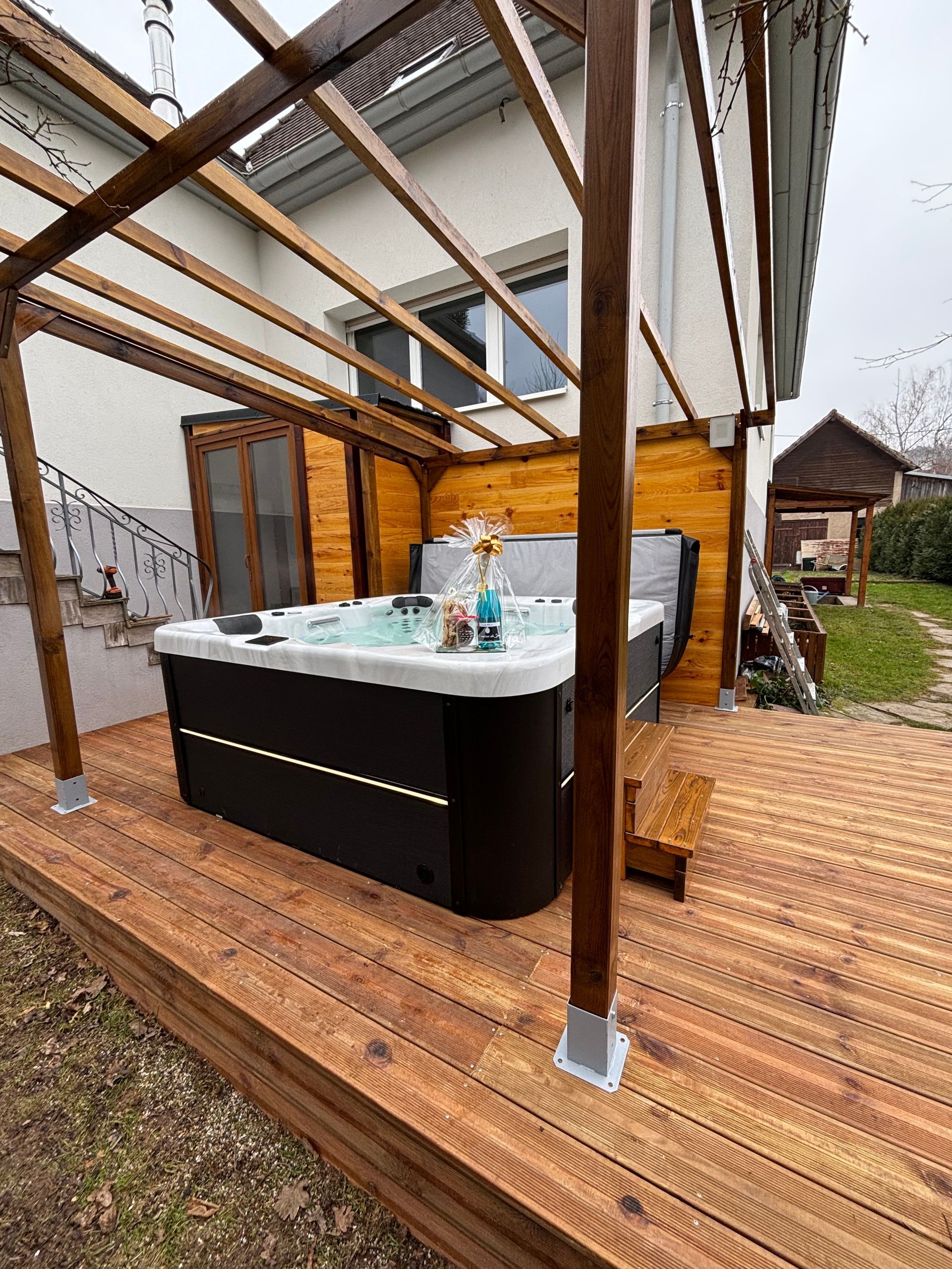 Un bain à remous est installé sur une terrasse en bois devant une maison.