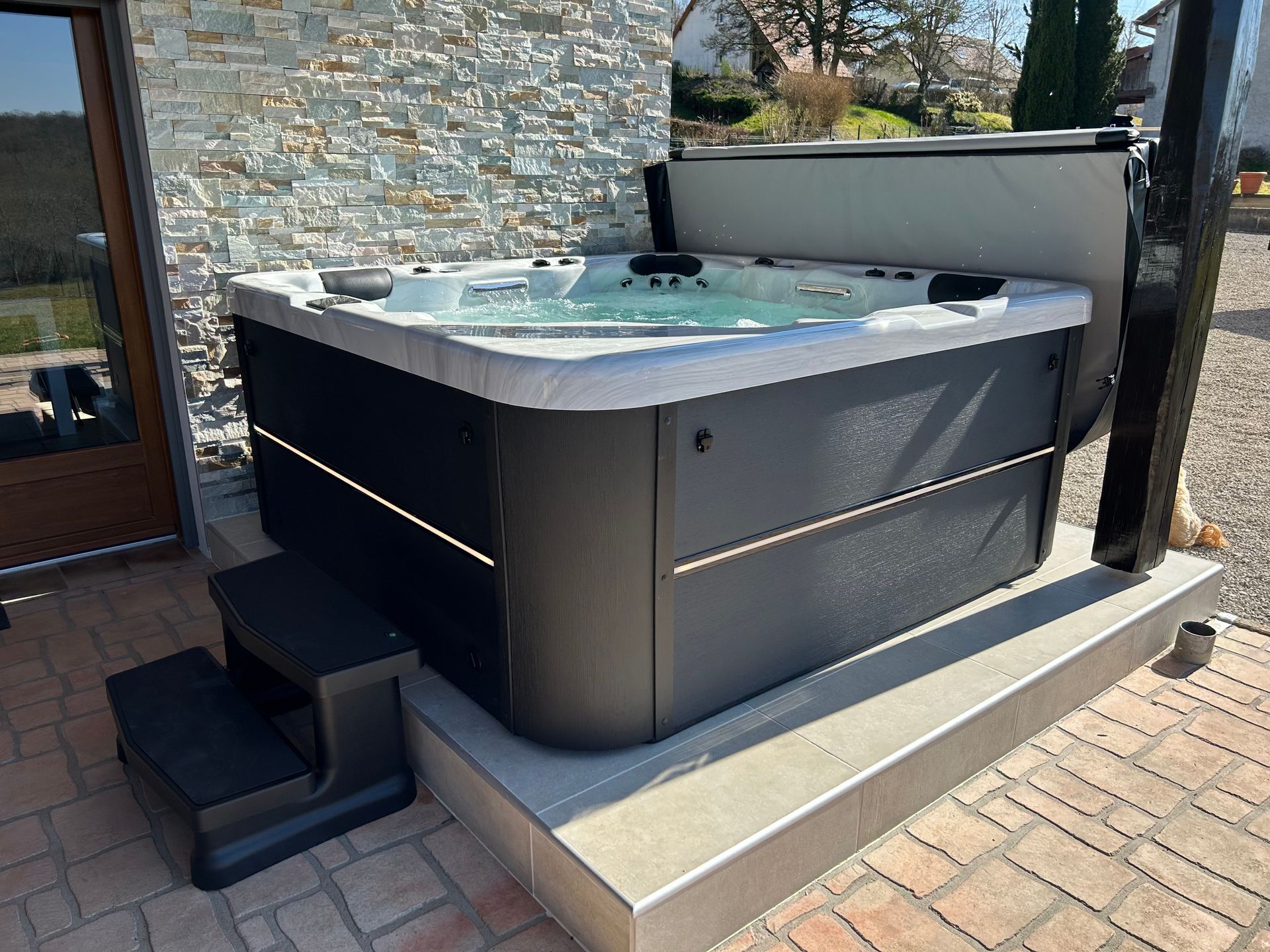 Un bain à remous est installé sur un patio en briques à côté d'un mur en pierre.