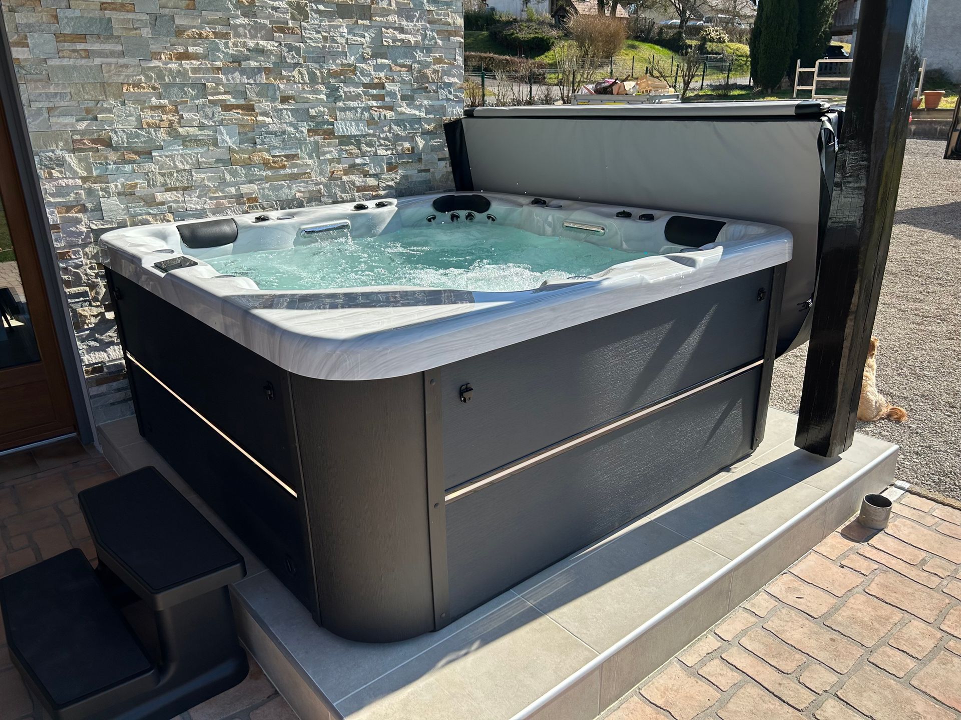 Un bain à remous est installé sur un patio en briques à côté d'un mur en pierre.