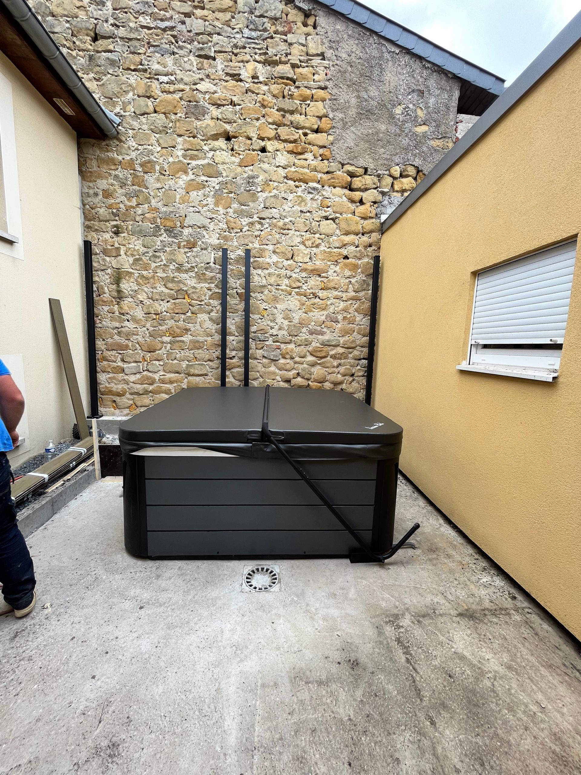 Un homme se tient à côté d'un bain à remous devant un mur de pierre.