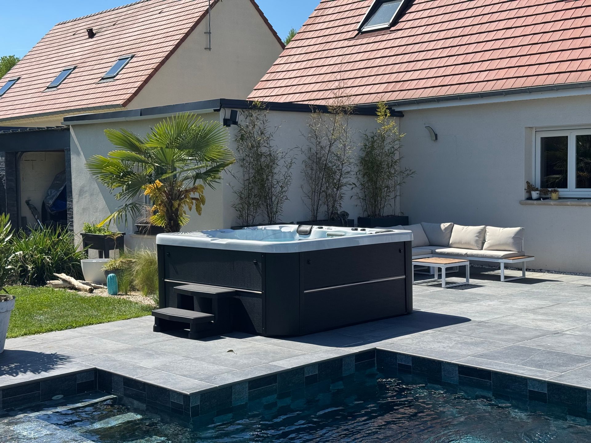 Un jacuzzi est installé à côté d'une piscine devant une maison.