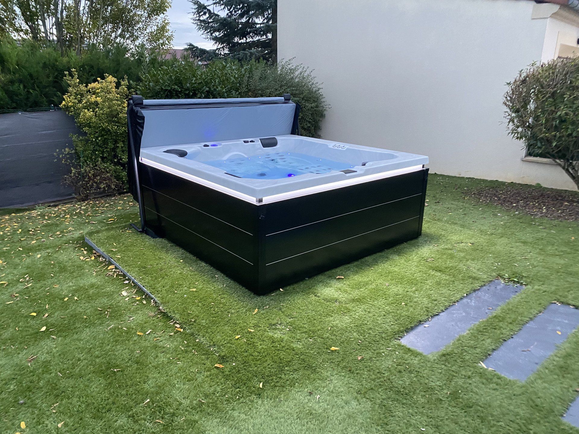 Un jacuzzi noir est posé sur une pelouse verte luxuriante.