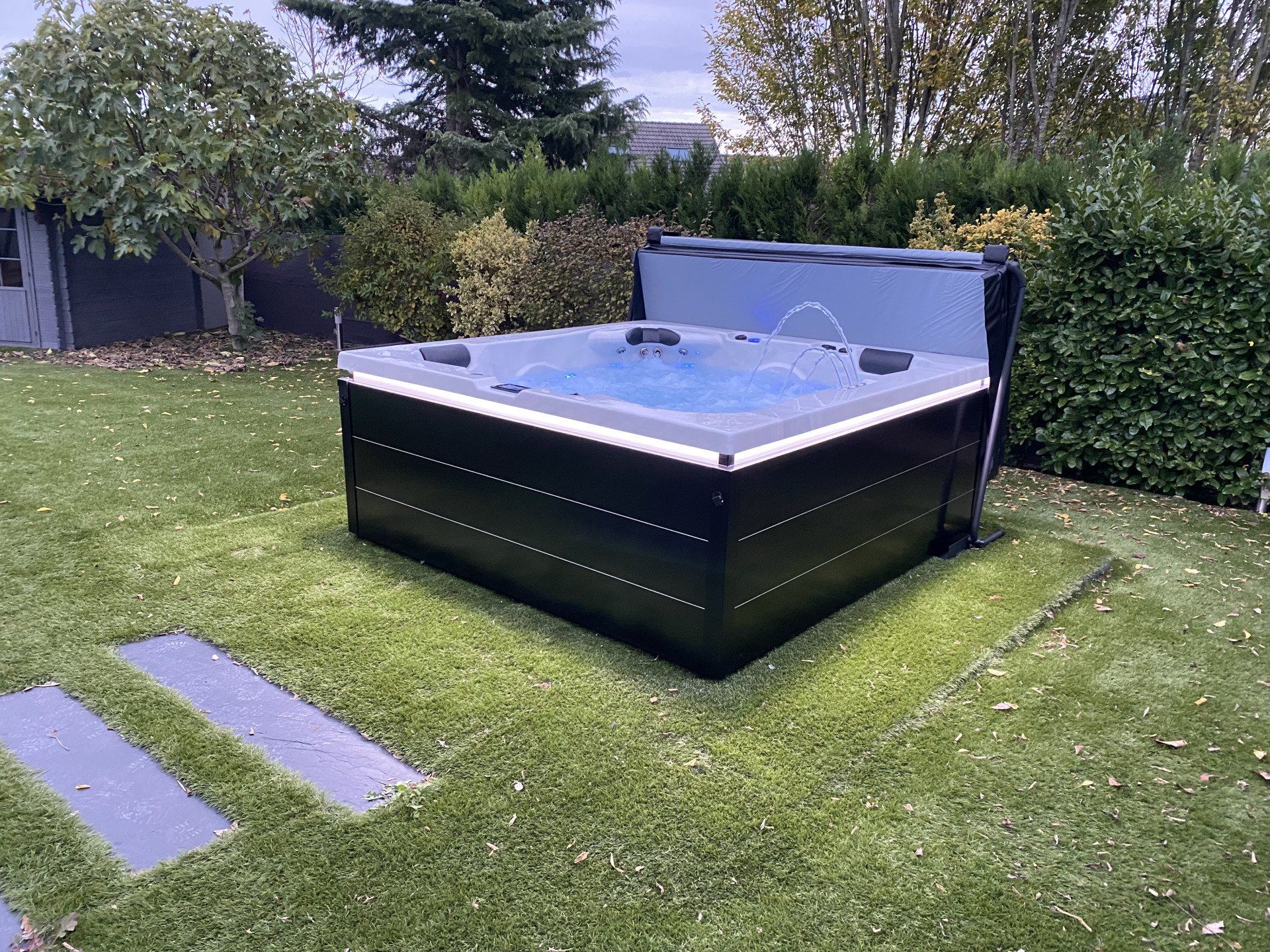 Un jacuzzi noir est posé sur une pelouse verte luxuriante.