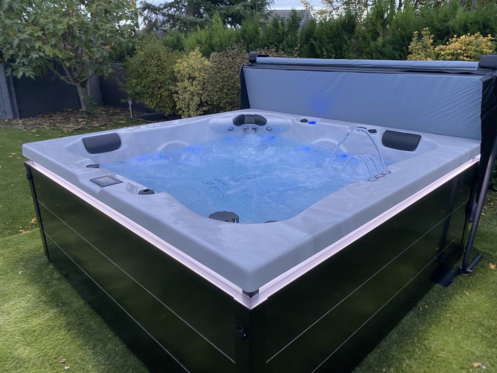 Un grand bain à remous carré est posé sur une pelouse verte luxuriante.