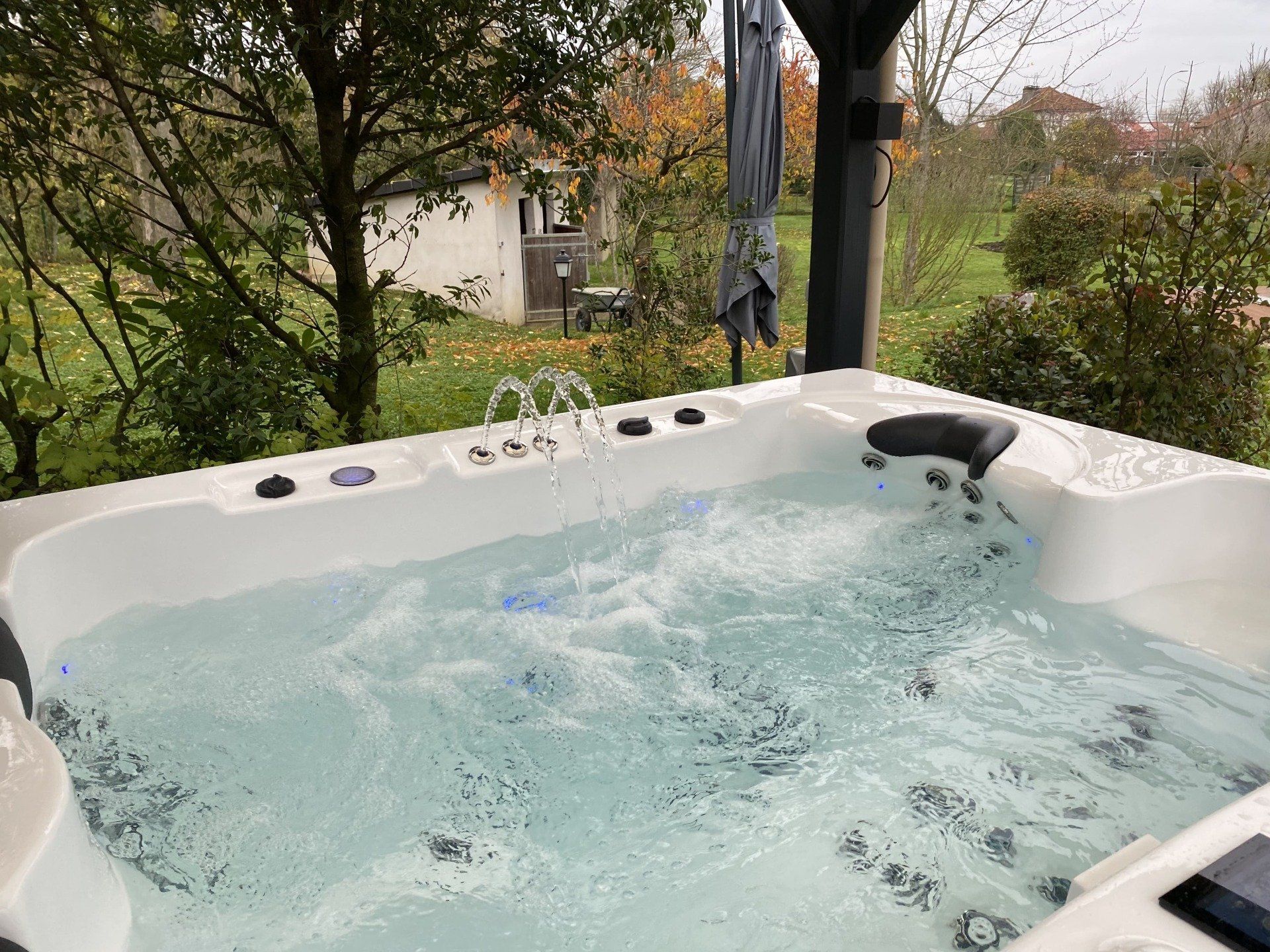 Un bain à remous rempli d'eau est placé sous un auvent dans un jardin.