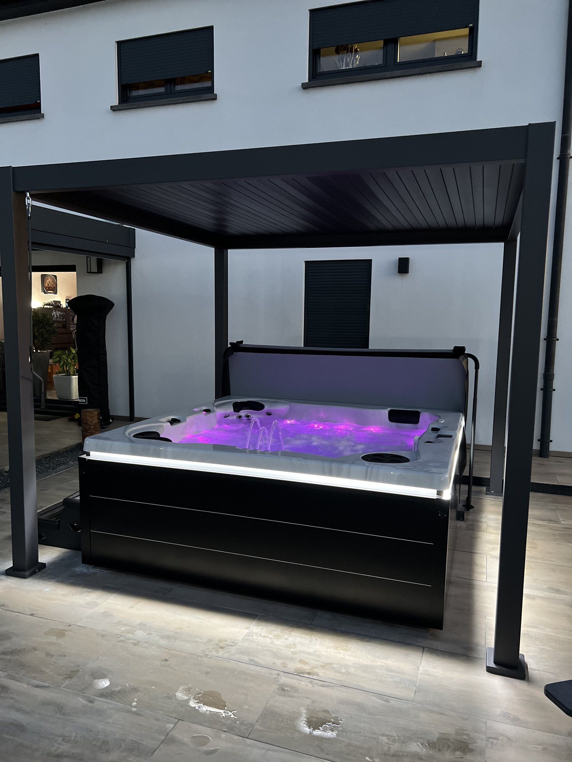 Un jacuzzi noir se trouve sous une pergola devant une maison