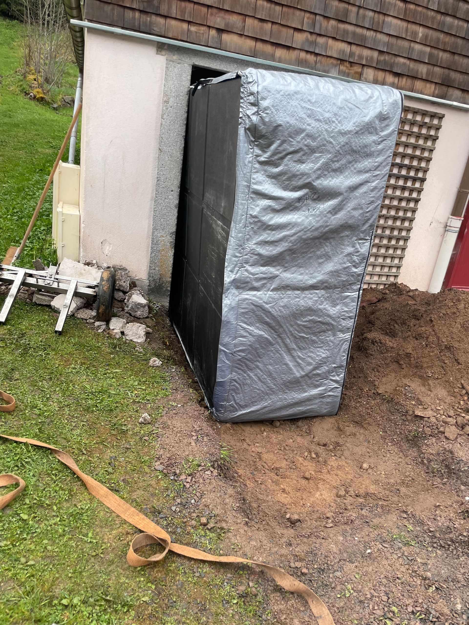 Un matelas est enveloppé dans une bâche et posé dans la terre devant un bâtiment.