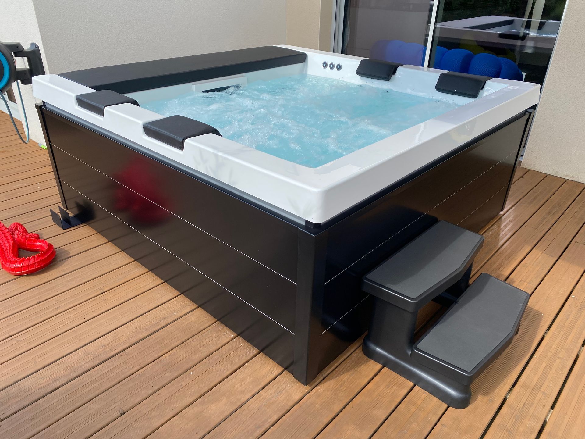 Un jacuzzi noir et blanc est posé sur une terrasse en bois.