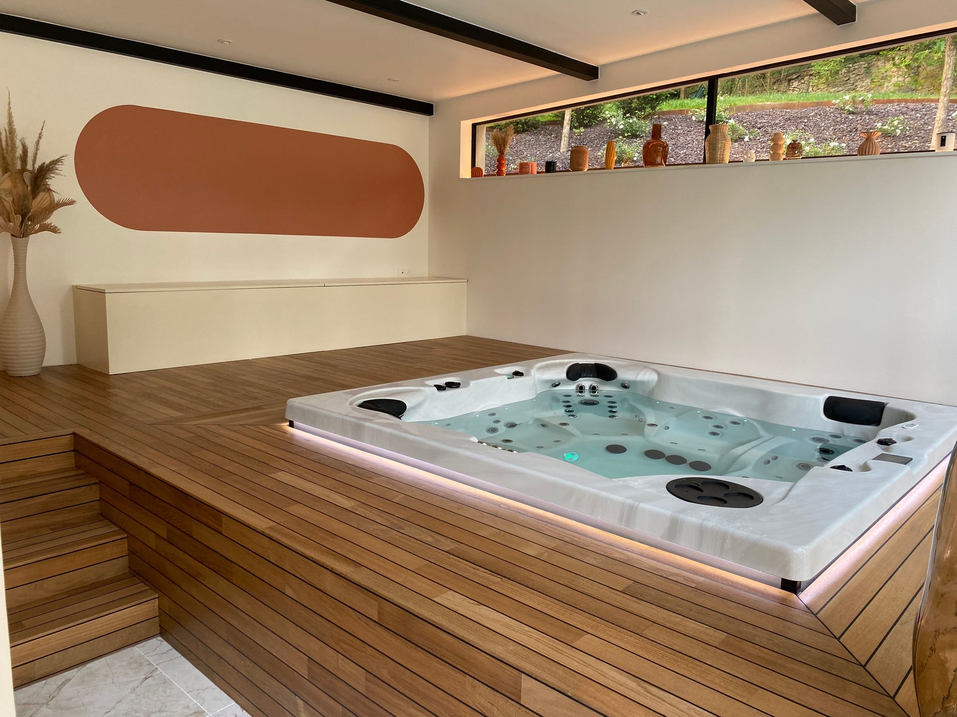 Un grand bain à remous est posé sur une terrasse en bois dans une pièce.