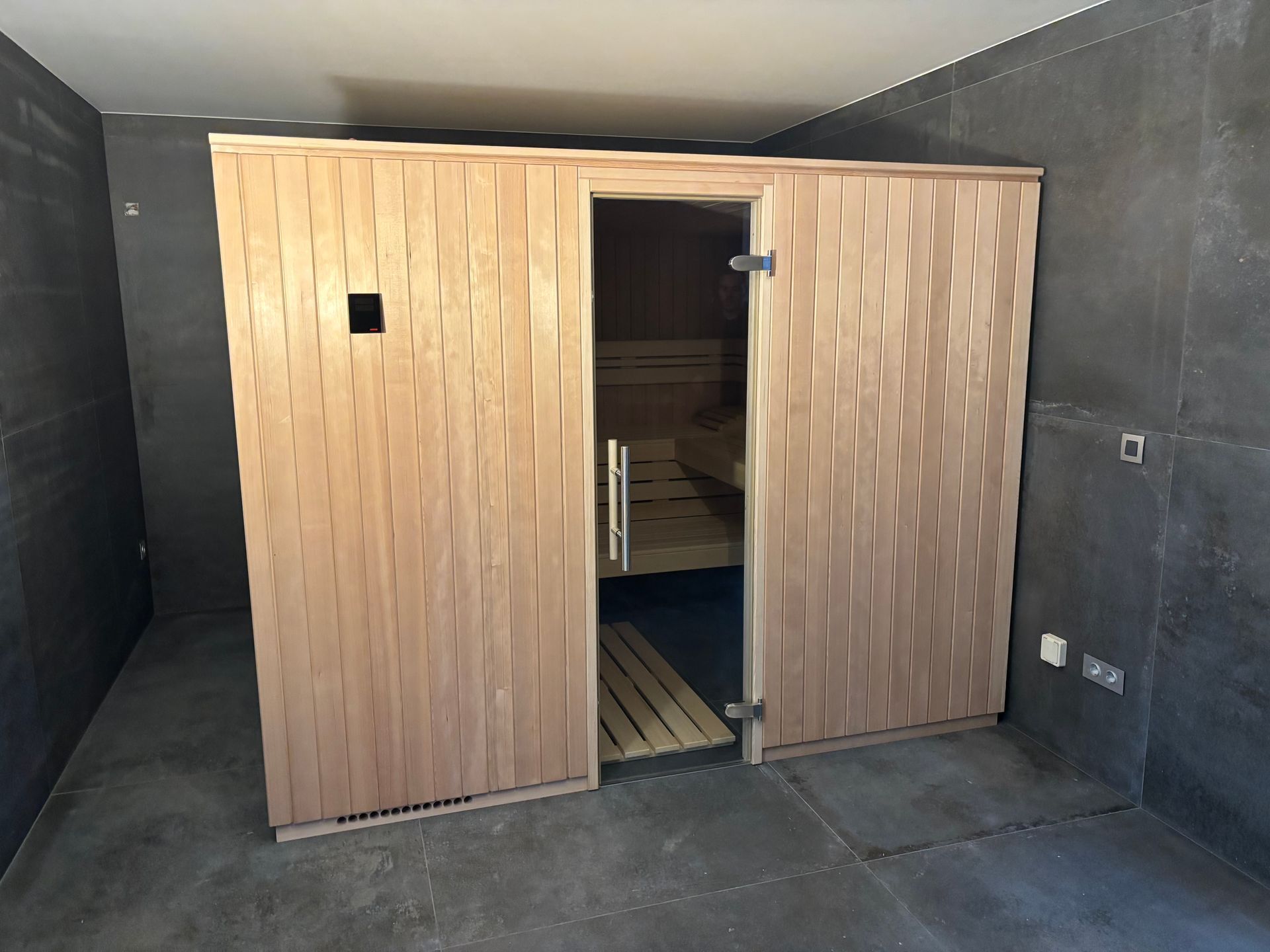 Sauna en bois avec porte ouverte dans une pièce aux murs et au sol sombres.