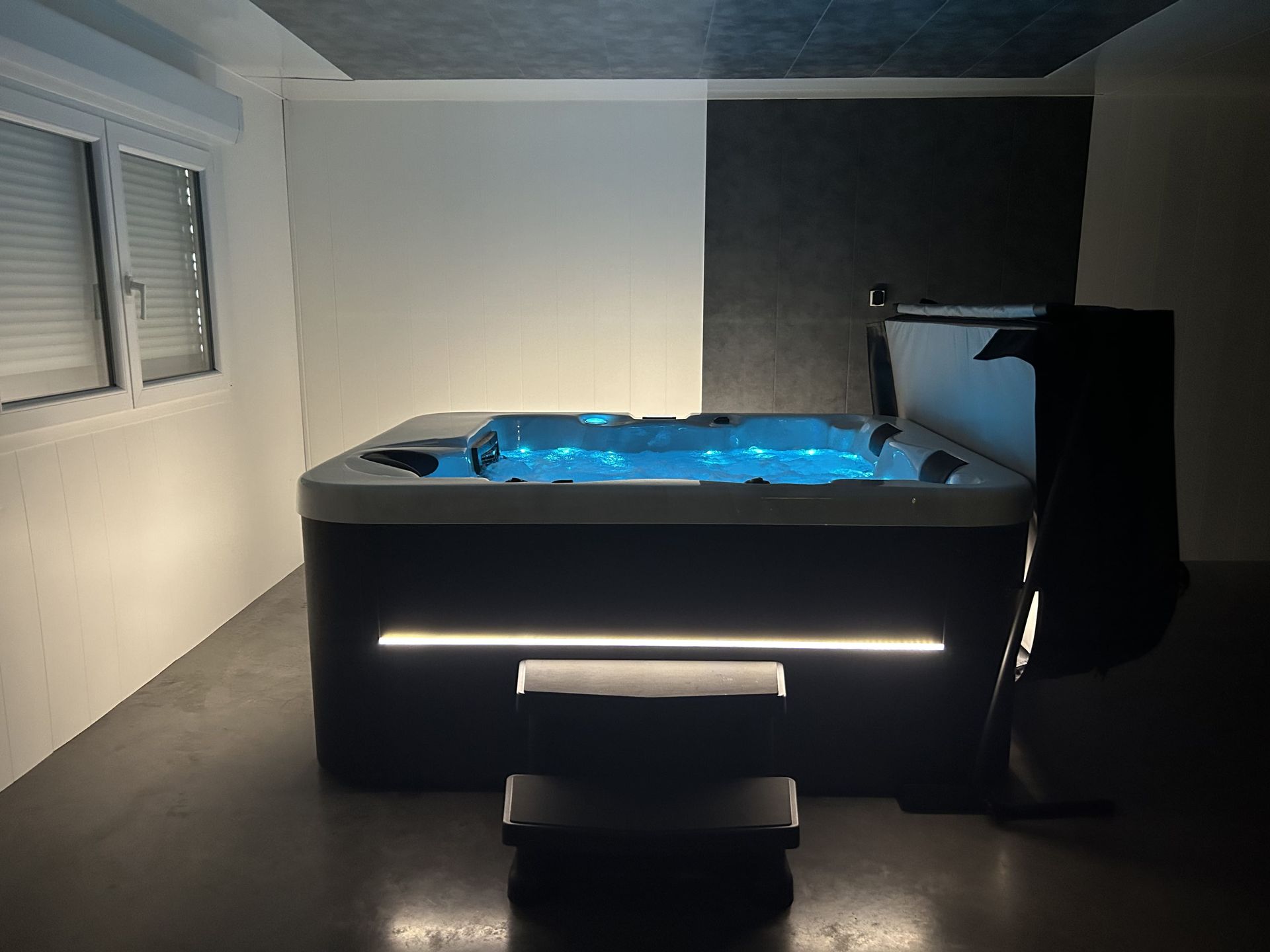 Un bain à remous est installé dans une pièce sombre à côté d'une fenêtre.