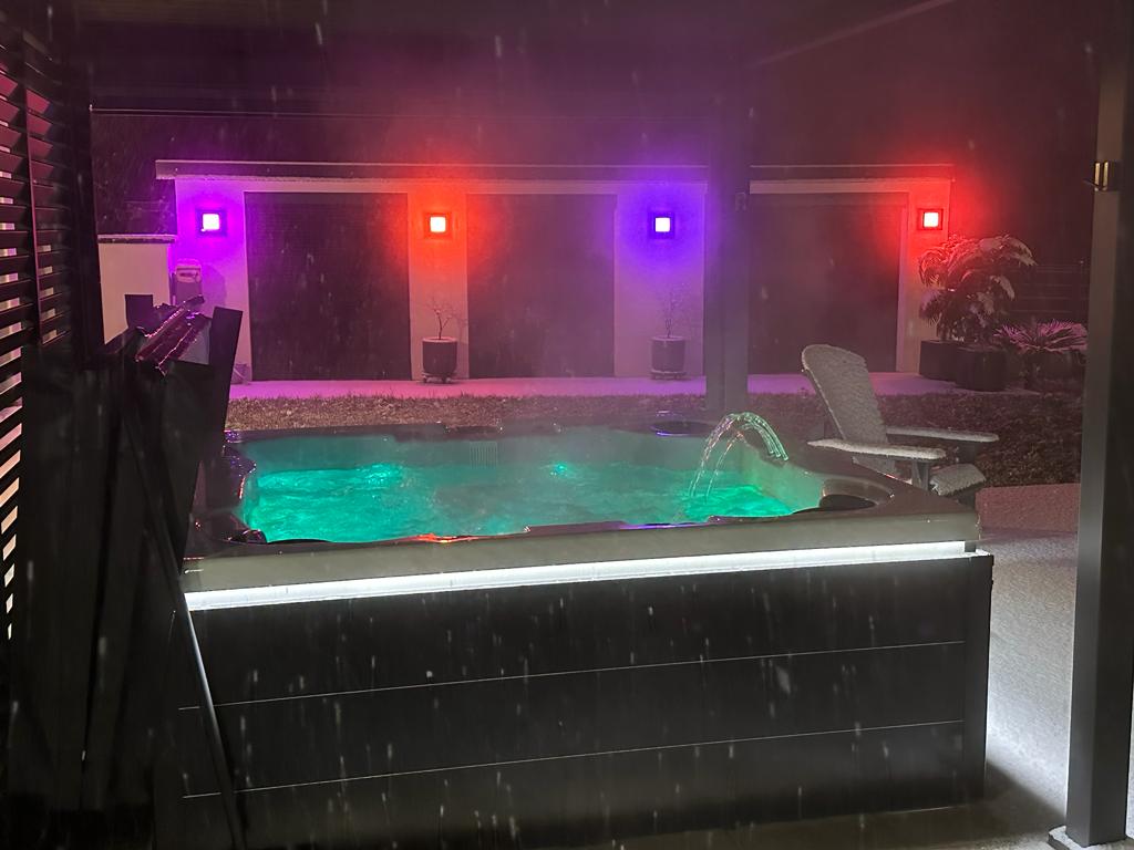 Un bain à remous est éclairé la nuit avec des lumières violettes et rouges.