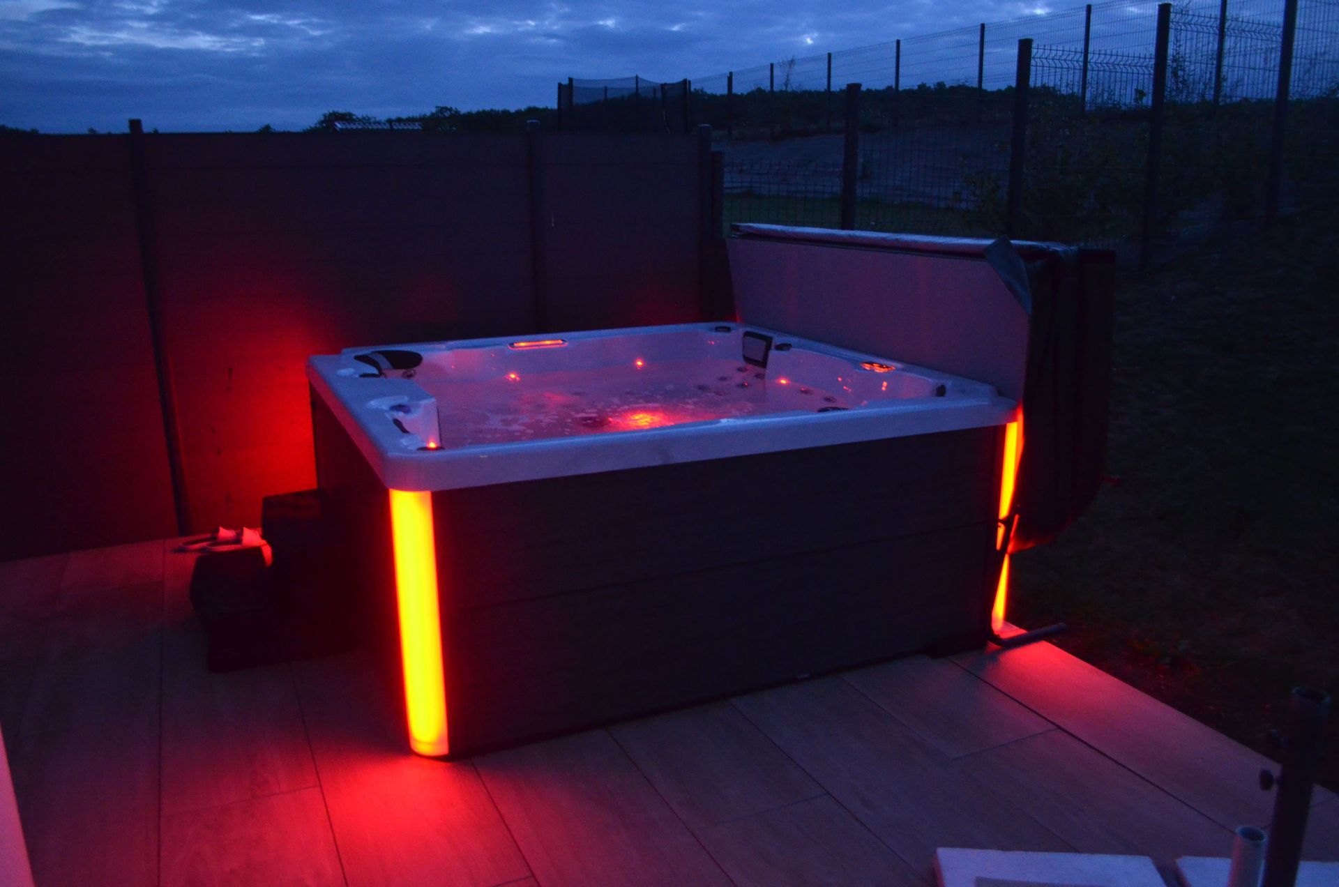 Un jacuzzi est éclairé la nuit sur une terrasse.