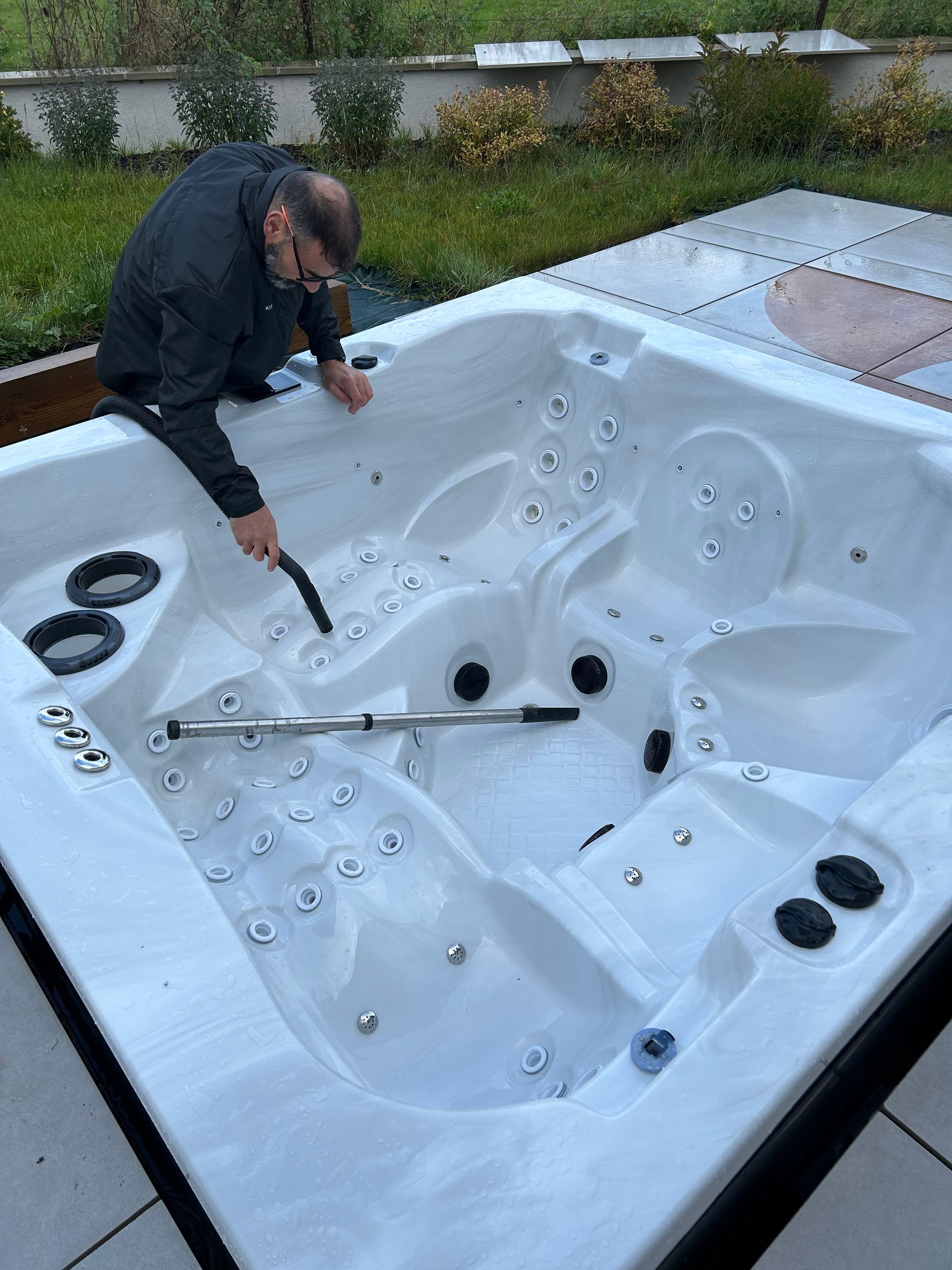 Un homme nettoie un jacuzzi avec un aspirateur.