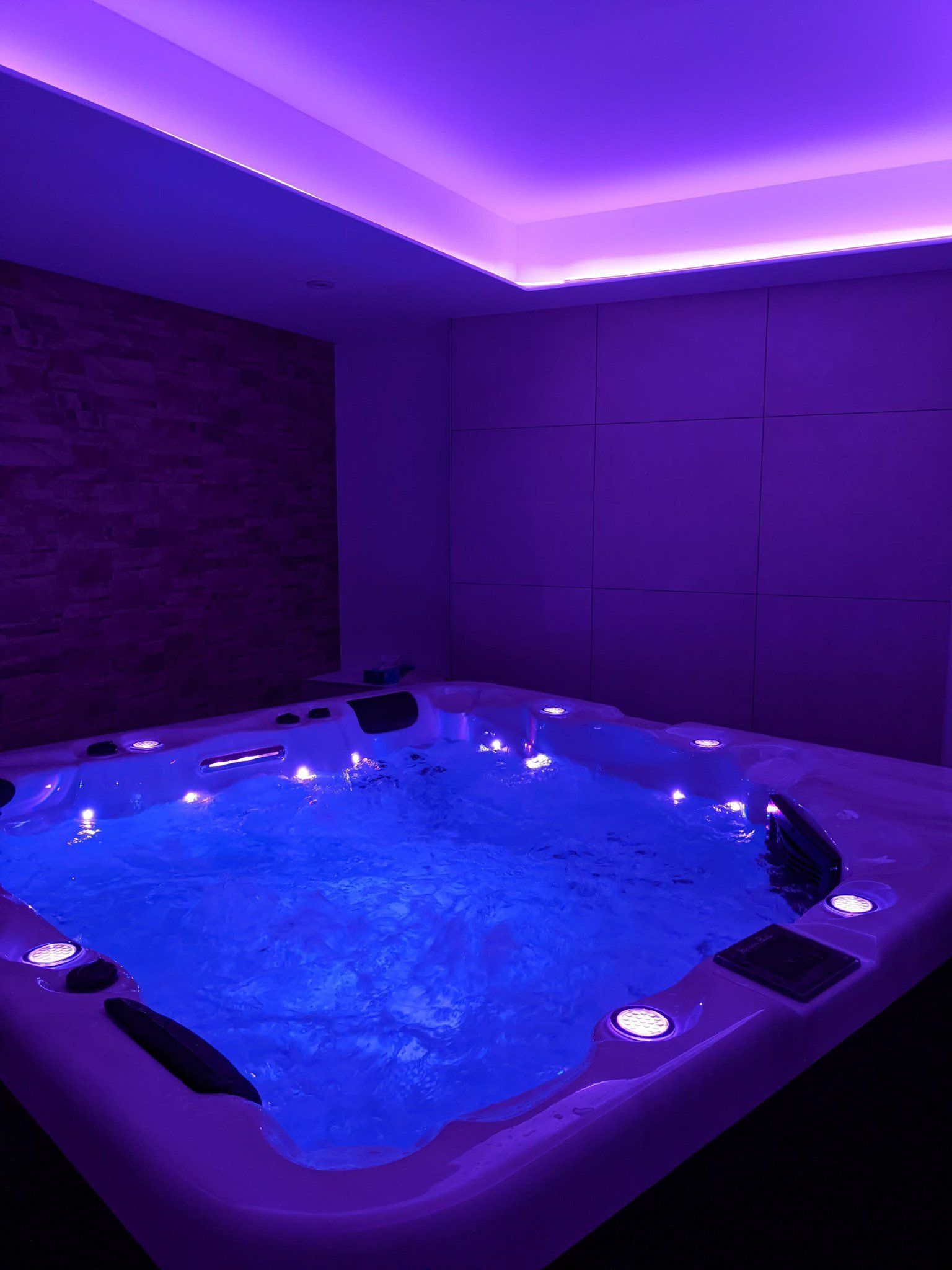Un bain à remous est installé dans une pièce avec des lumières violettes au plafond.