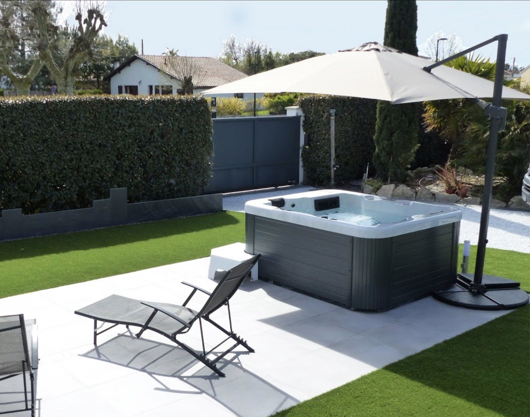 Un jacuzzi est installé sous un parasol dans un jardin