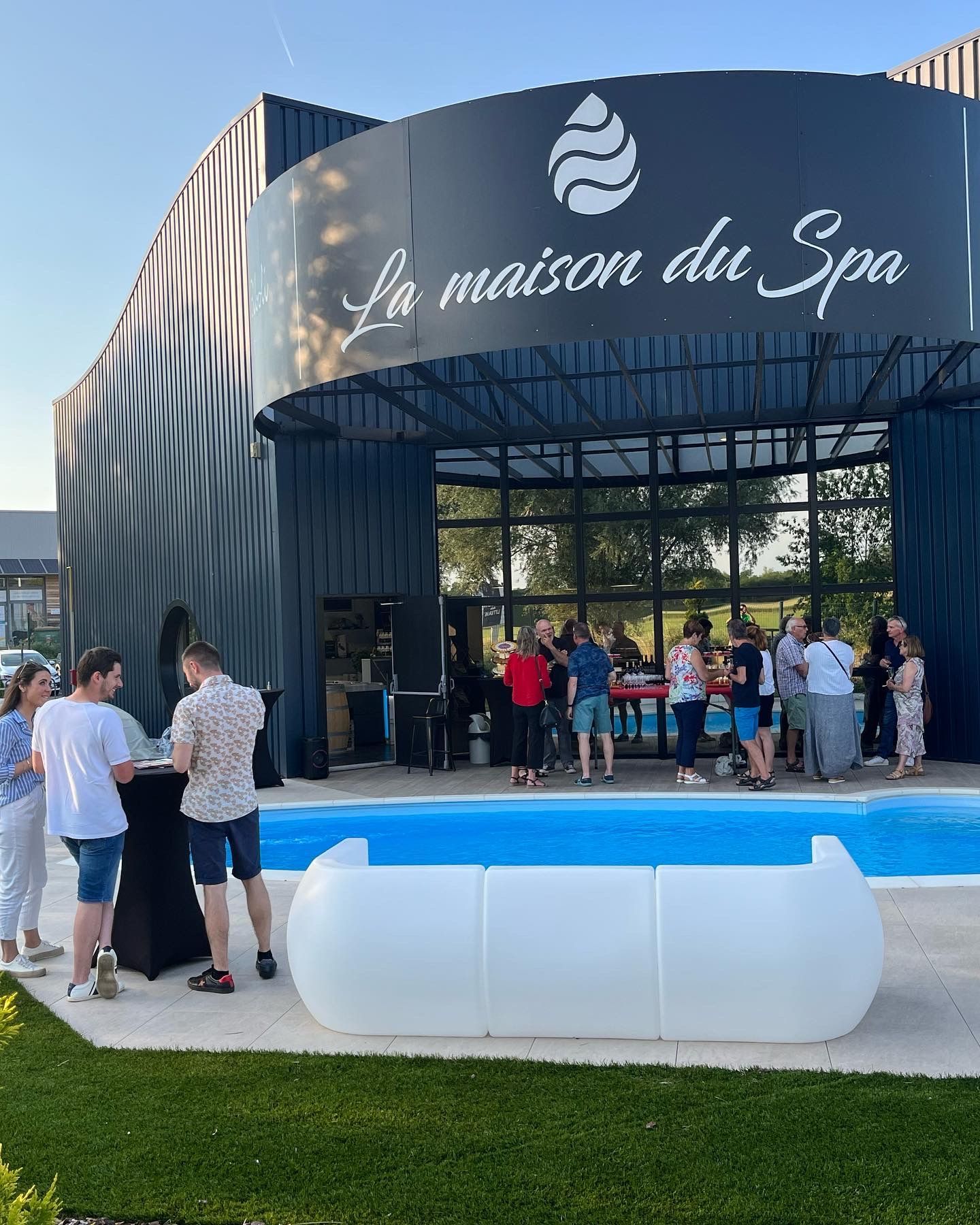 Un groupe de personnes se tient autour d'une piscine devant un bâtiment.