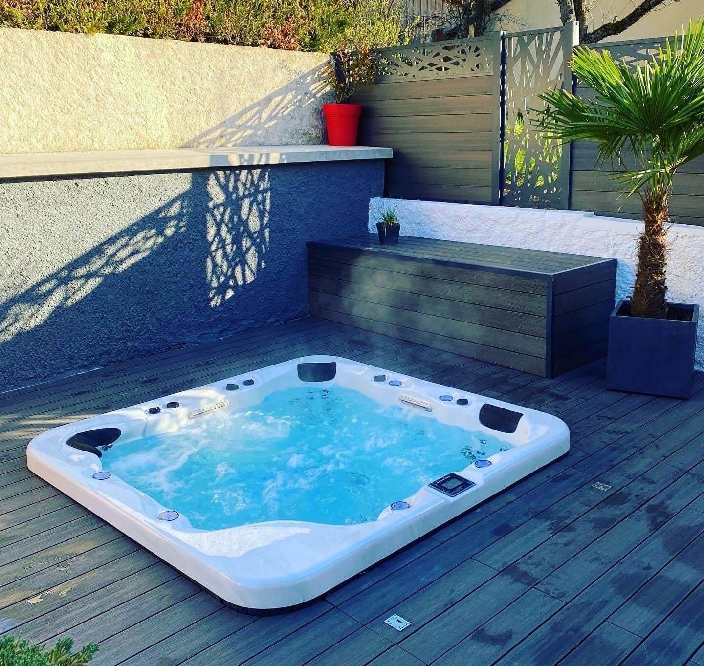 Un bain à remous blanc est posé sur une terrasse en bois.