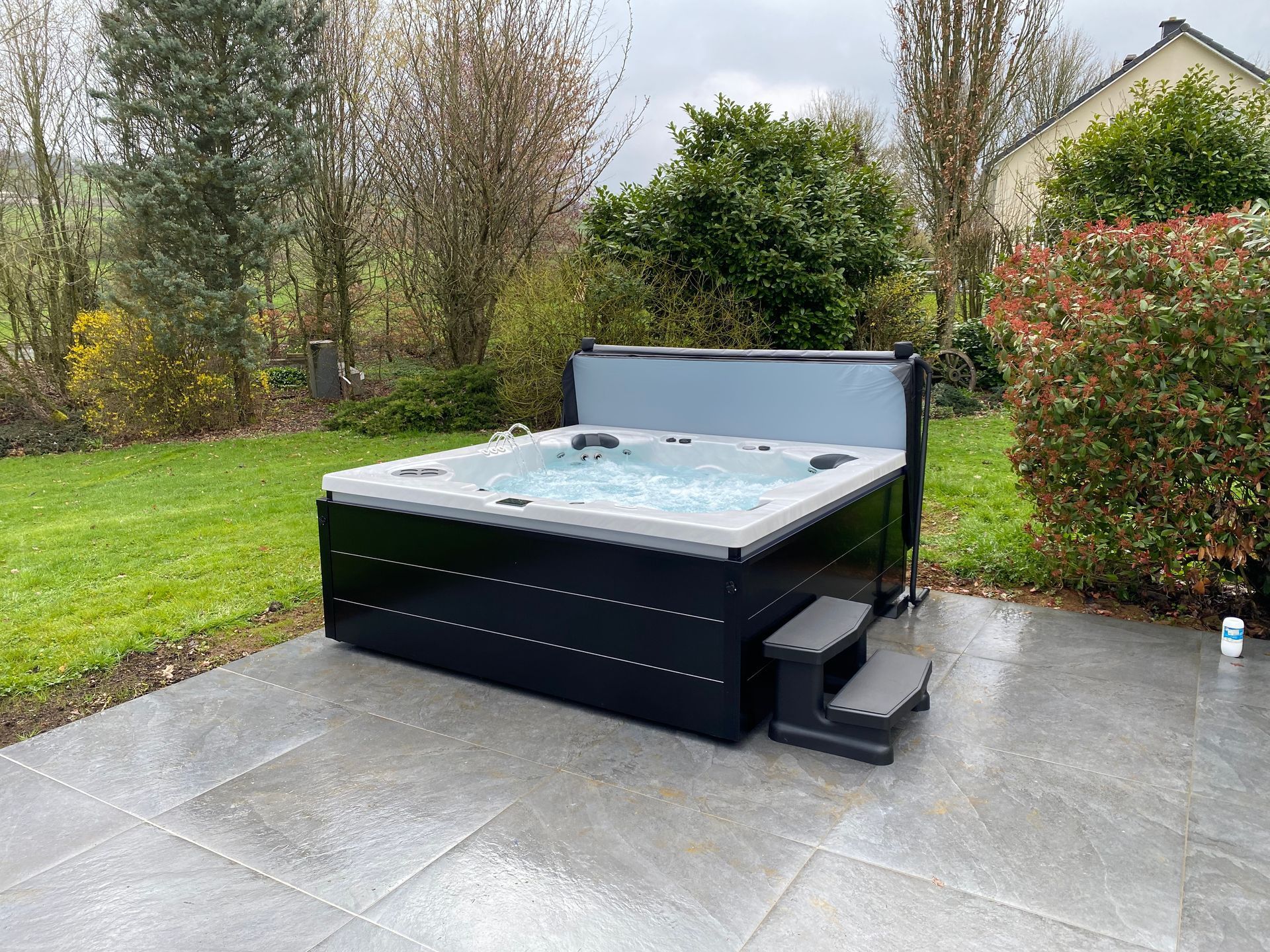 Un jacuzzi noir est posé sur une terrasse dans une cour arrière.
