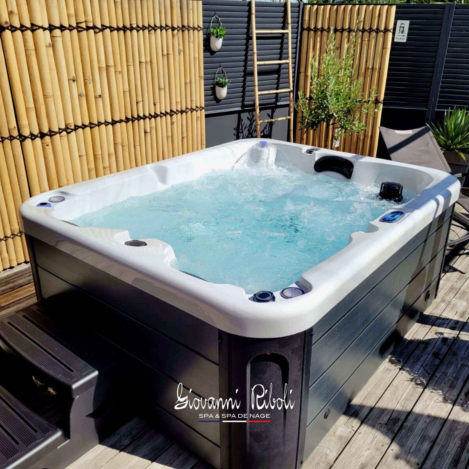 Un bain à remous est installé sur une terrasse en bois à côté d'une clôture en bambou.