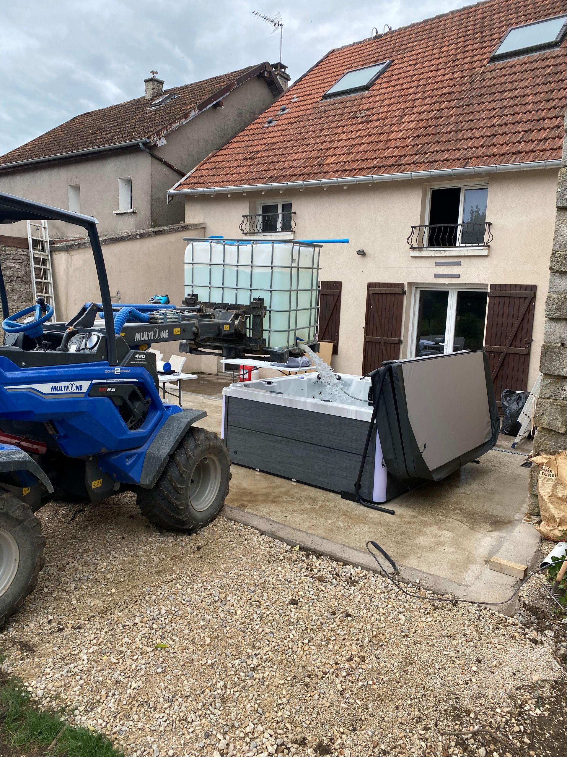 Un tracteur transporte un jacuzzi devant une maison.