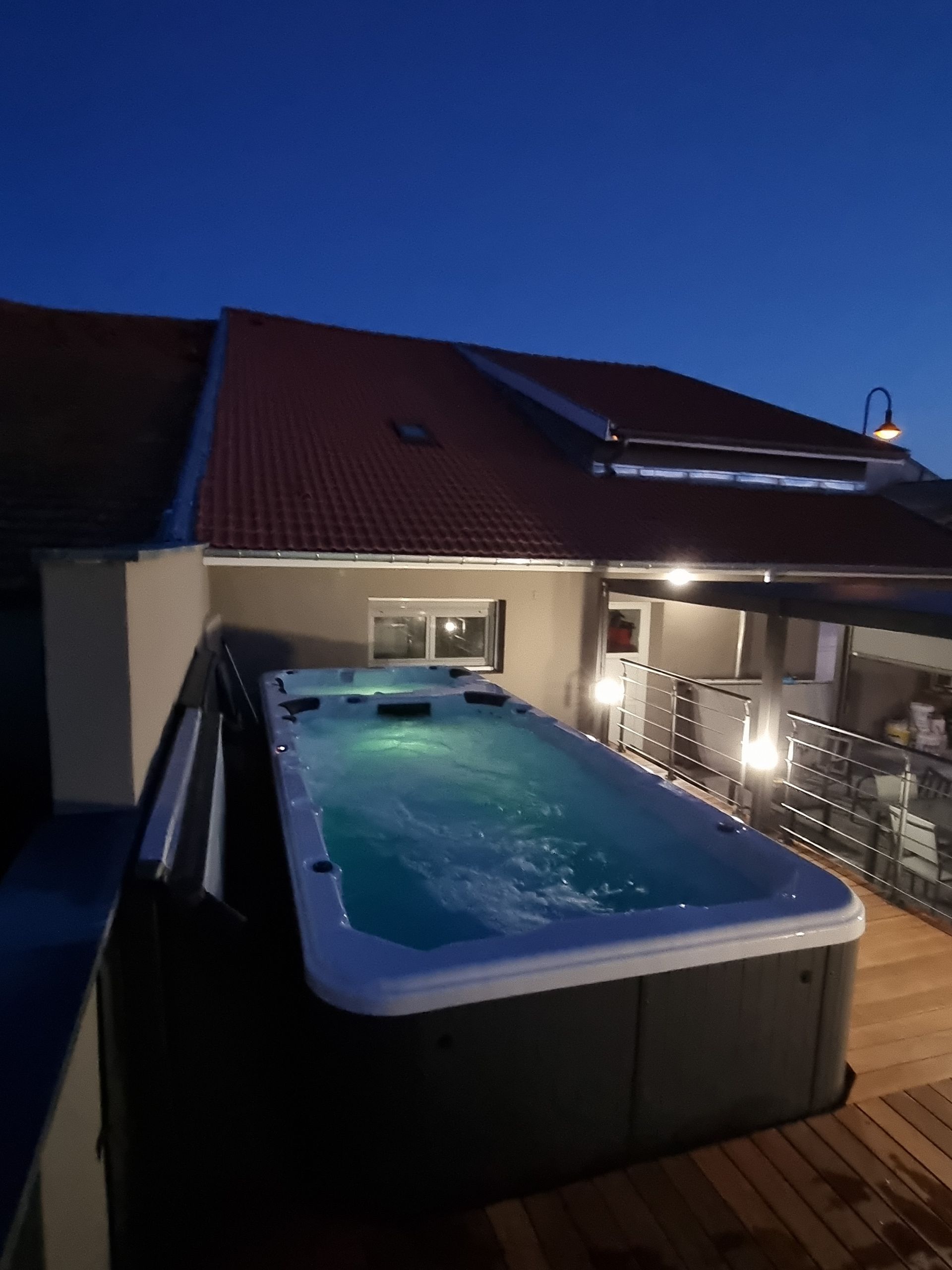 Une grande piscine est éclairée la nuit devant une maison.